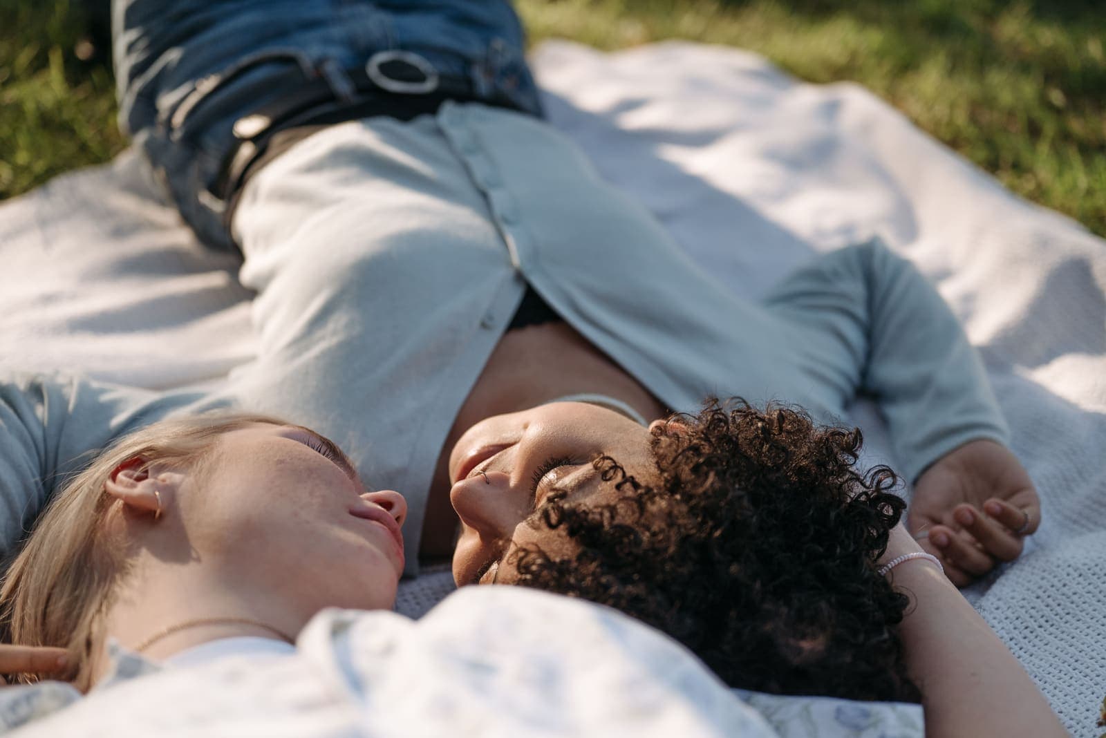 A couple lying close together on a blanket in the sunlight, faces turned toward each other in a tender moment