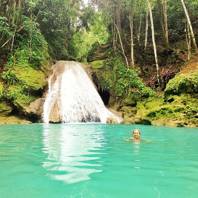 A lush jungle waterfall spilling into a turquoise natural swimming pool in Jamaica
